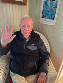 An old person sitting in a chair waving
Description automatically generated